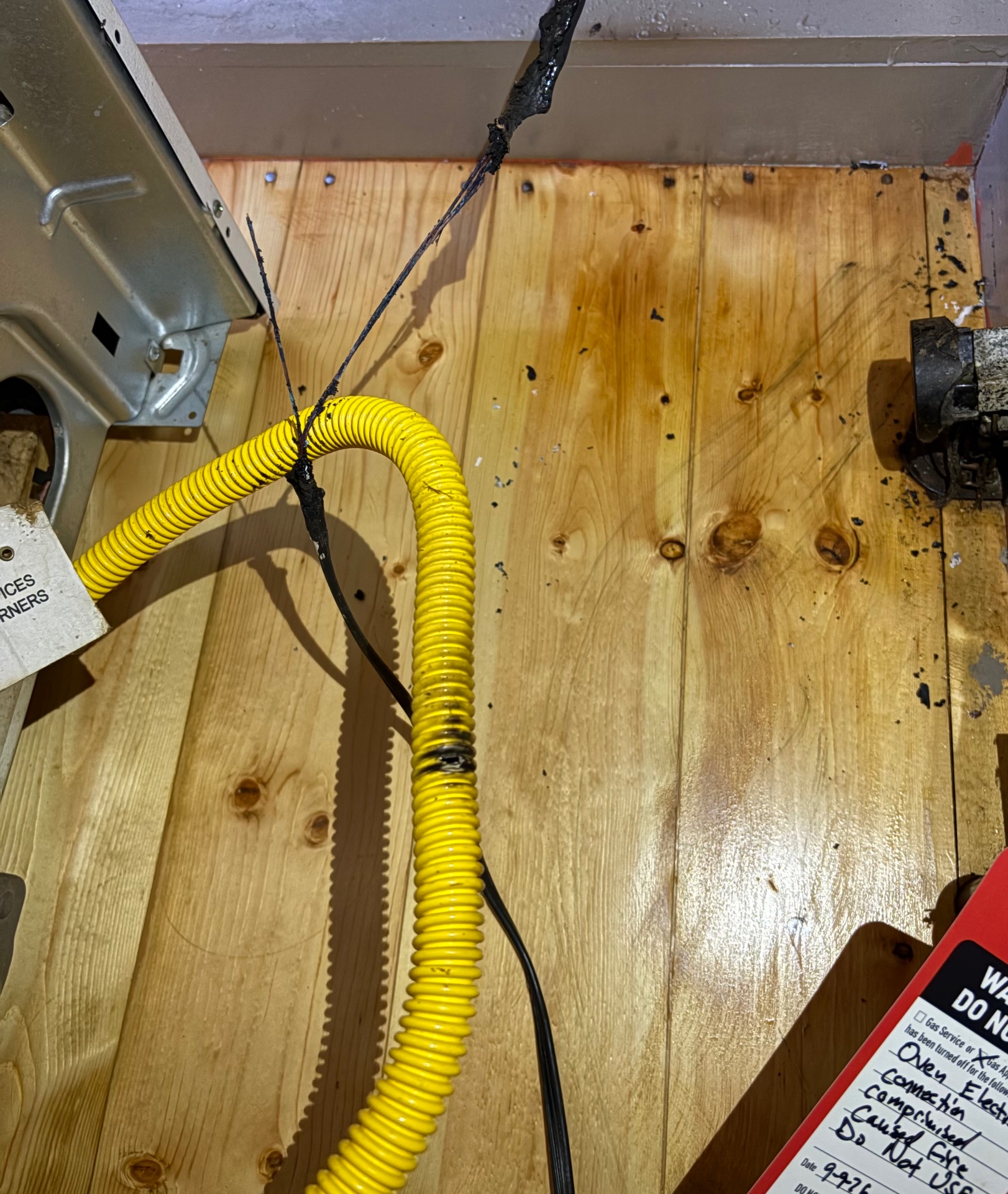 Melted and arced range power cord lying across a yellow gas line that it punctured, documented during a Knapp's service call in the Portland area.
